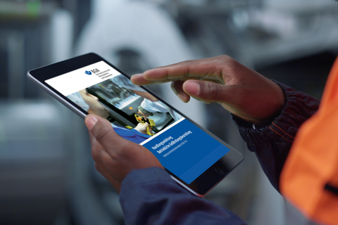  Ein Mann in Arbeitskleidung hält in einer Produktionsanlage ein Tablet in der Hand